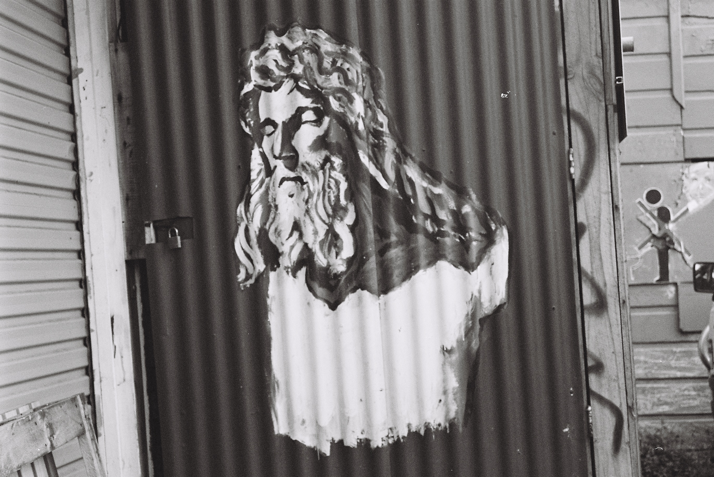 Black and white photo of a street art depiction of a bearded man. He looks a bit holy like White Jesus.