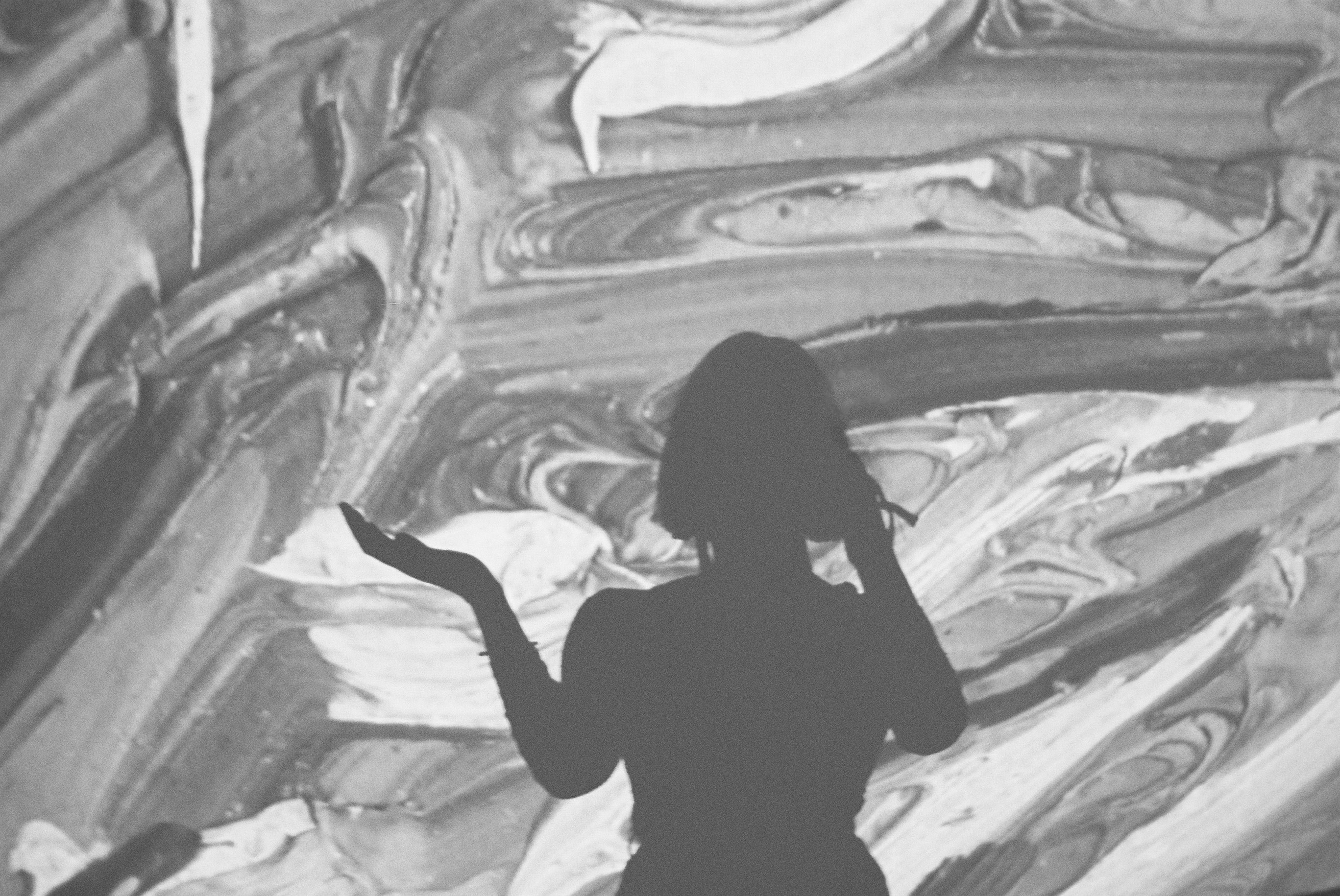 A black and white sillhouette of a person taking a photo. The background is gooey like when the coffee runs into the milk of an iced-coffee